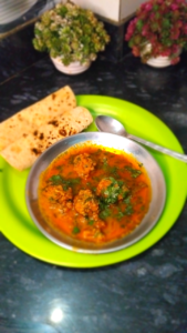 Sprinkling fresh coriander on Keema Kofta Curry before serving