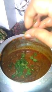 Fresh coriander leaves being added as garnish on hot Masala Kaleji curry