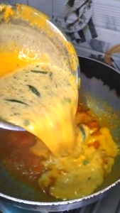 pouring kadhi mixture into tadka besan curd curry cooking process