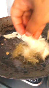 Adding namak para pieces one by one into hot oil for frying