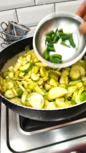 Adding Green Chilies, Turmeric and Salt to Ridge Gourd Recipe
